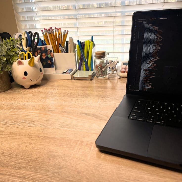 Cozy desk workspace with laptop displaying code, unicorn pen holder, and other stationery